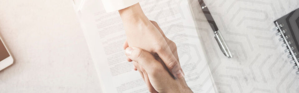 Two people shaking hands over a collaboration agreement.