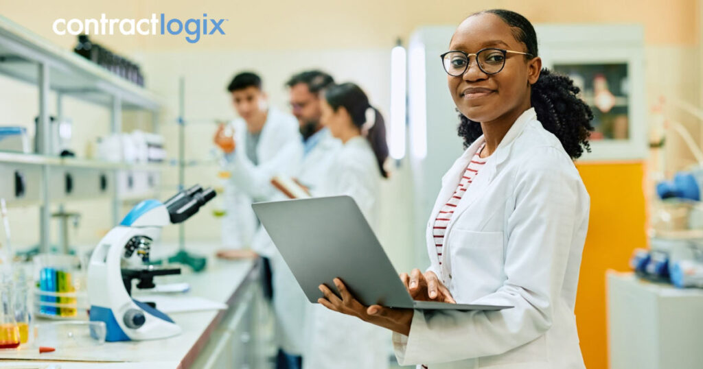 smiling woman in a modern lab, uses pharma contract management on her laptop