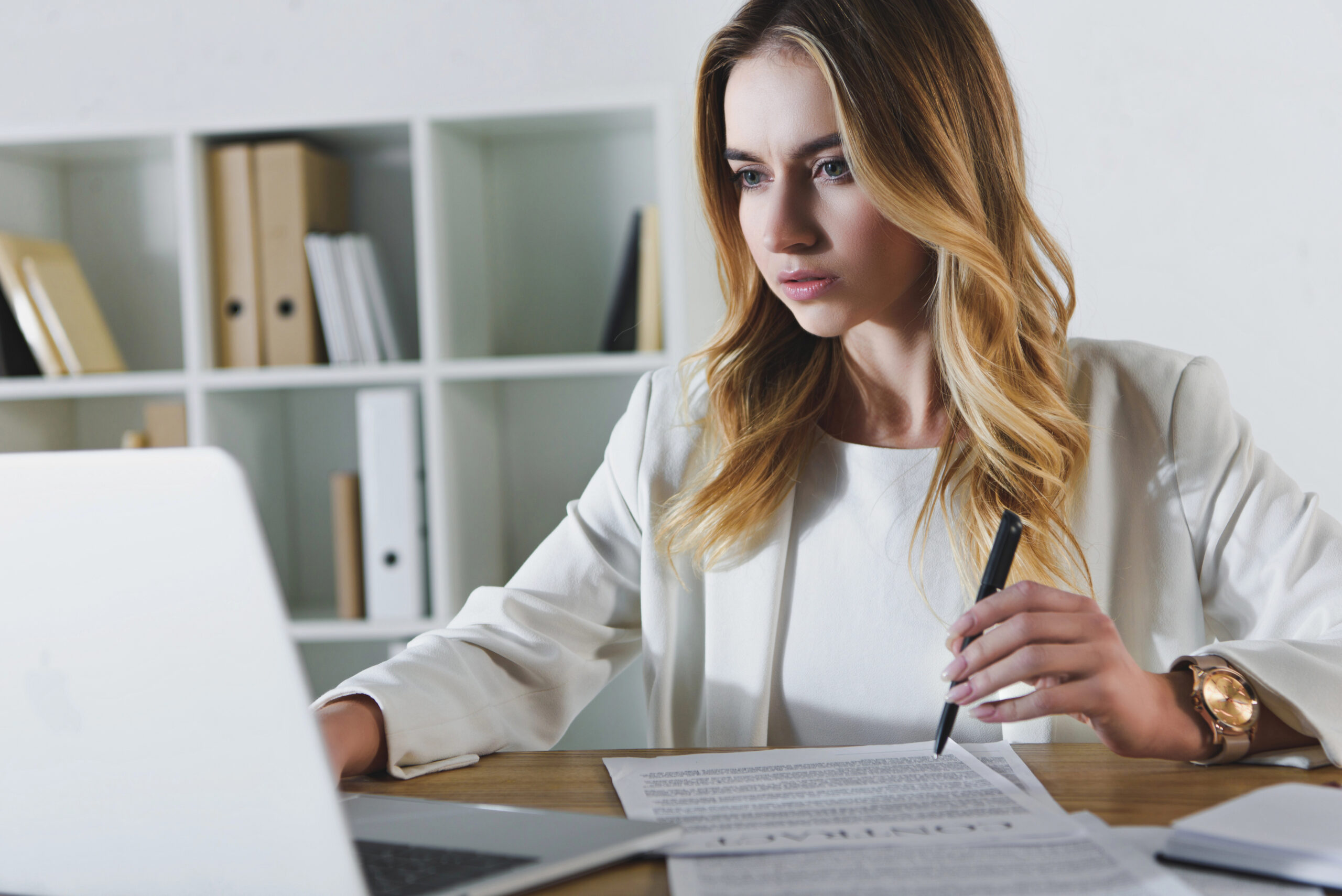 woman sitting at desk looking at laptop computer holding pen near contract learning how AI contract operations enhances business continuity