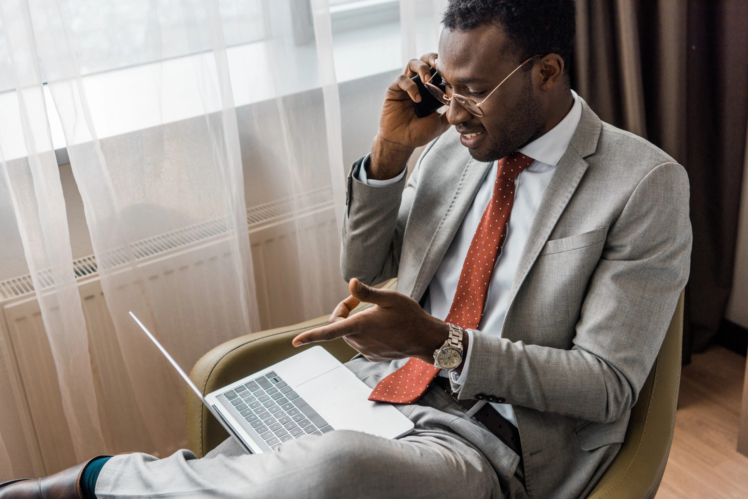 smiling businessman talking on smartphone and pointing at laptop while using contract management automation