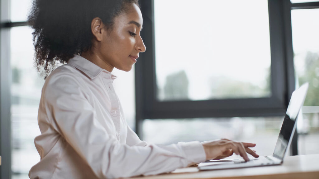 side view of woman sitting at desk using laptop computer to learn about contract management workflows