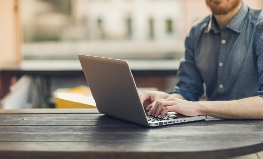 A man sits at a table, using his laptop to leverage contract management software for a smooth and efficient negotiation process